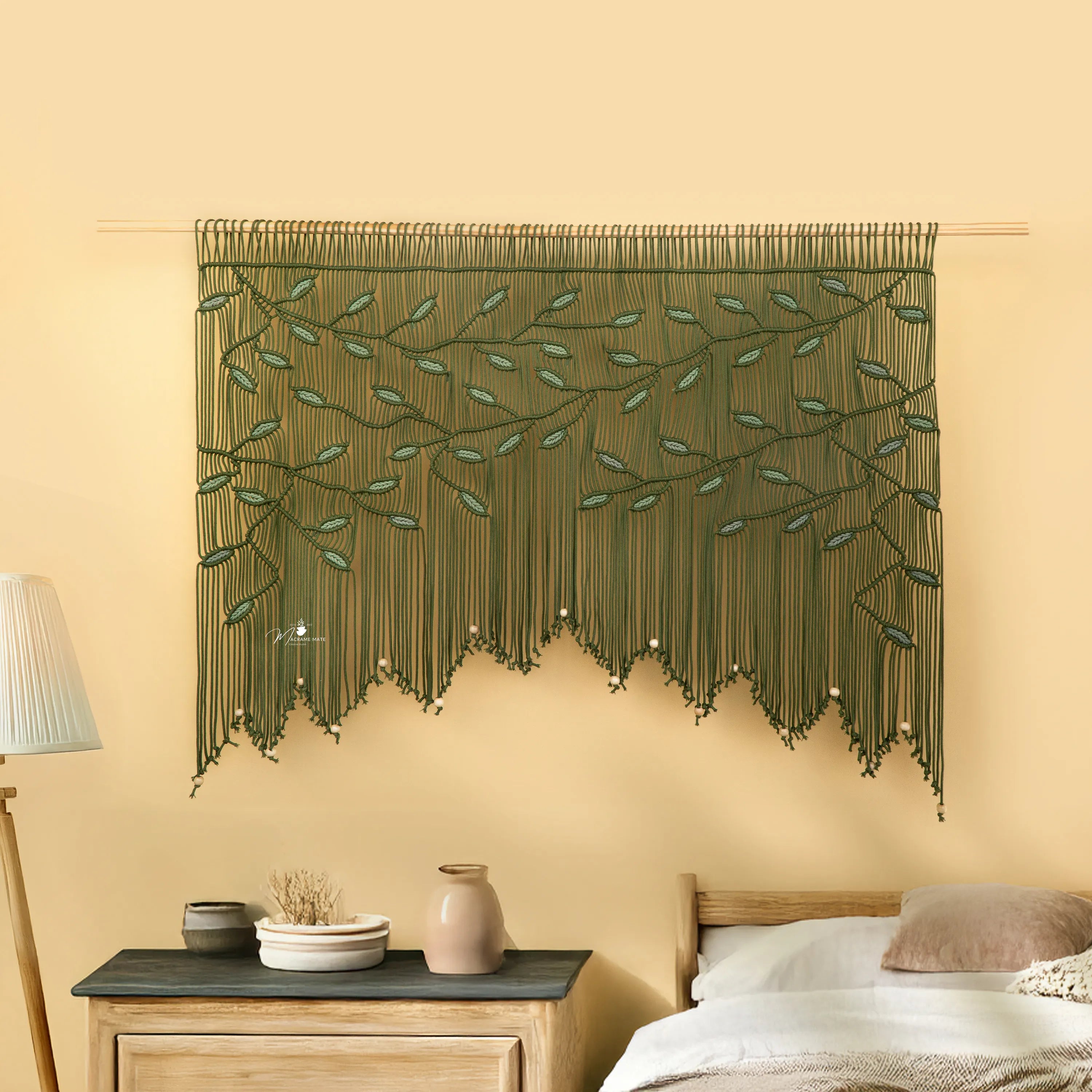 Decorative green wall hanging with leaf pattern on a beige wall above a bed.