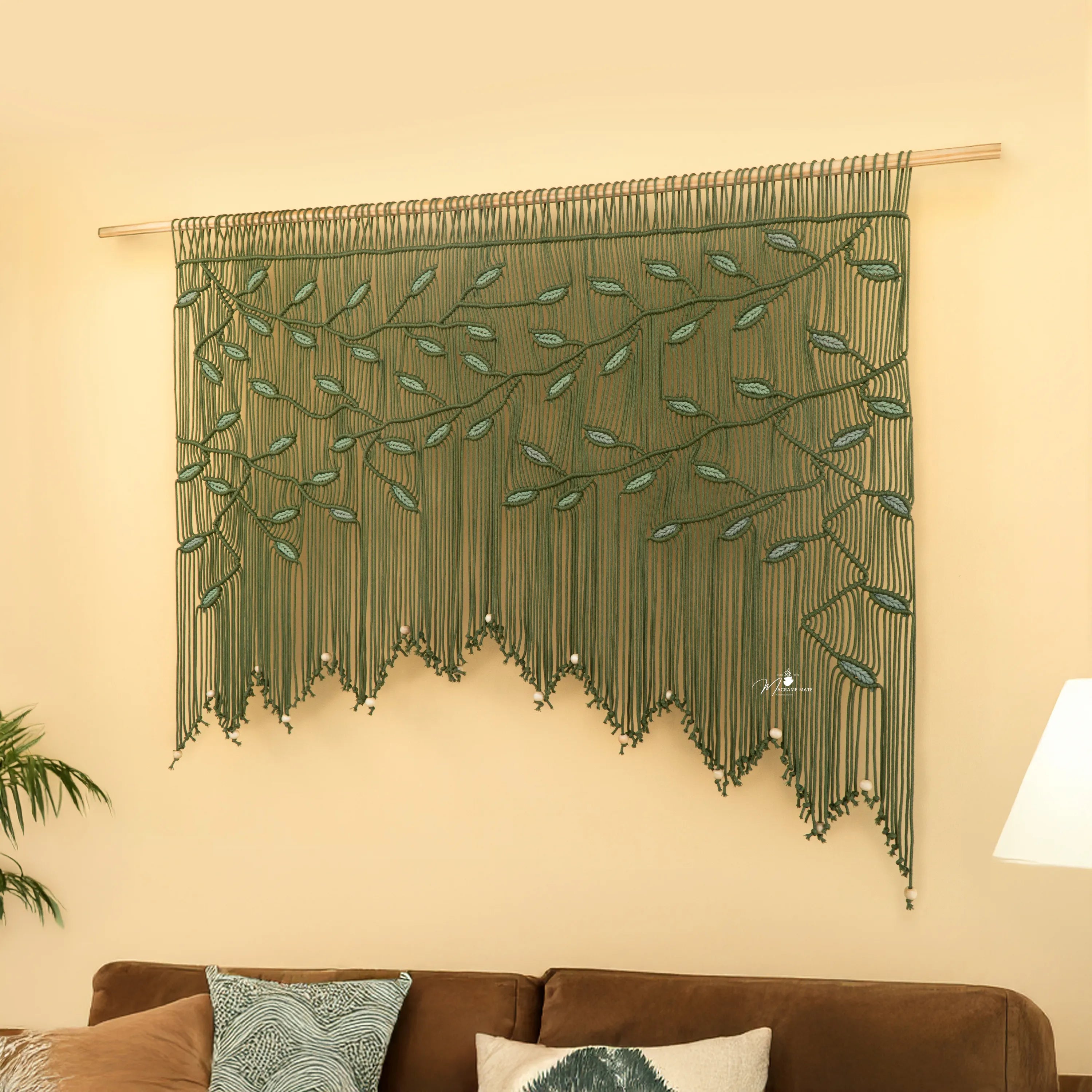 Decorative green wall hanging with leaf pattern on a beige wall above a brown sofa.