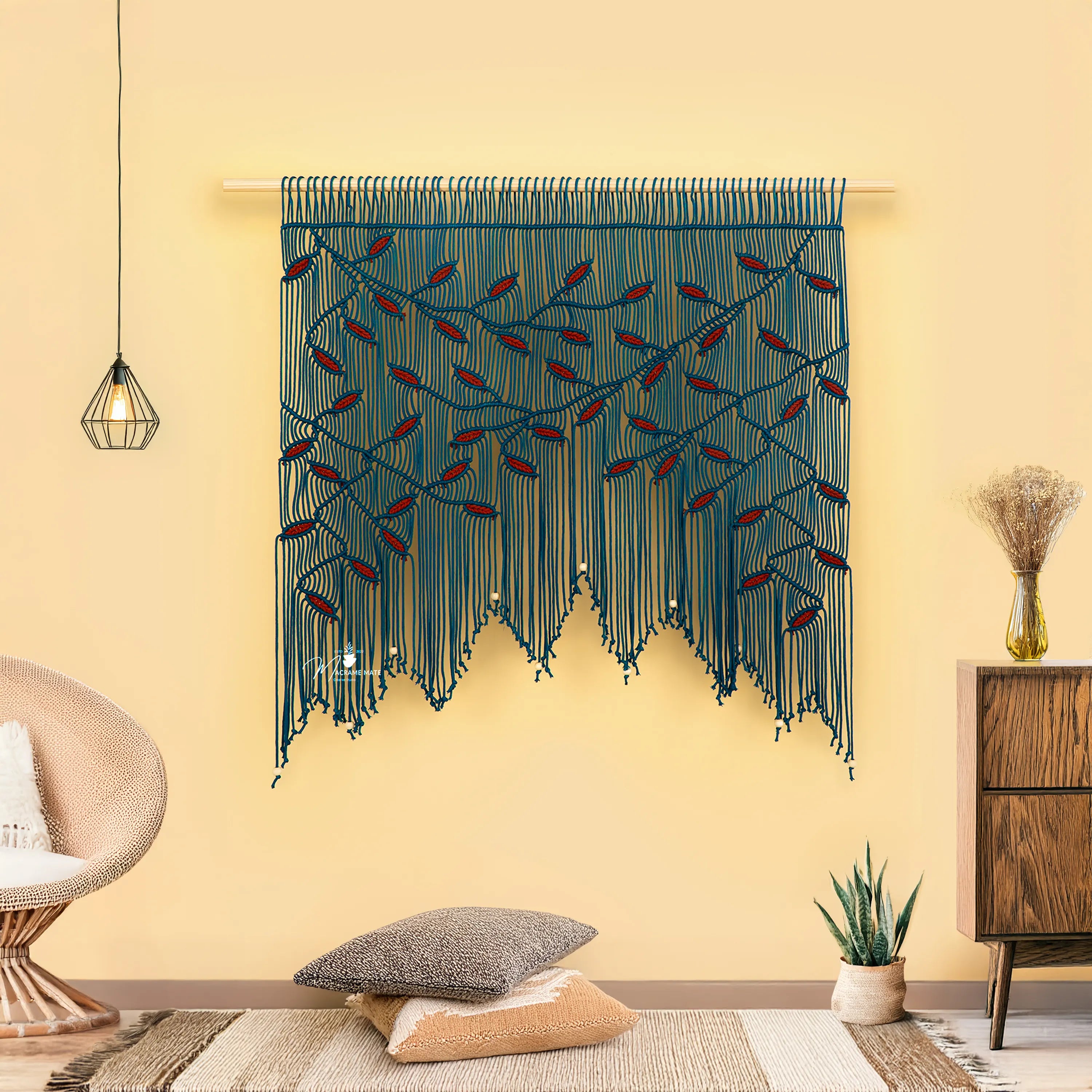 Decorative wall hanging with blue and red strings in a room with a chair, pillow, and plant.