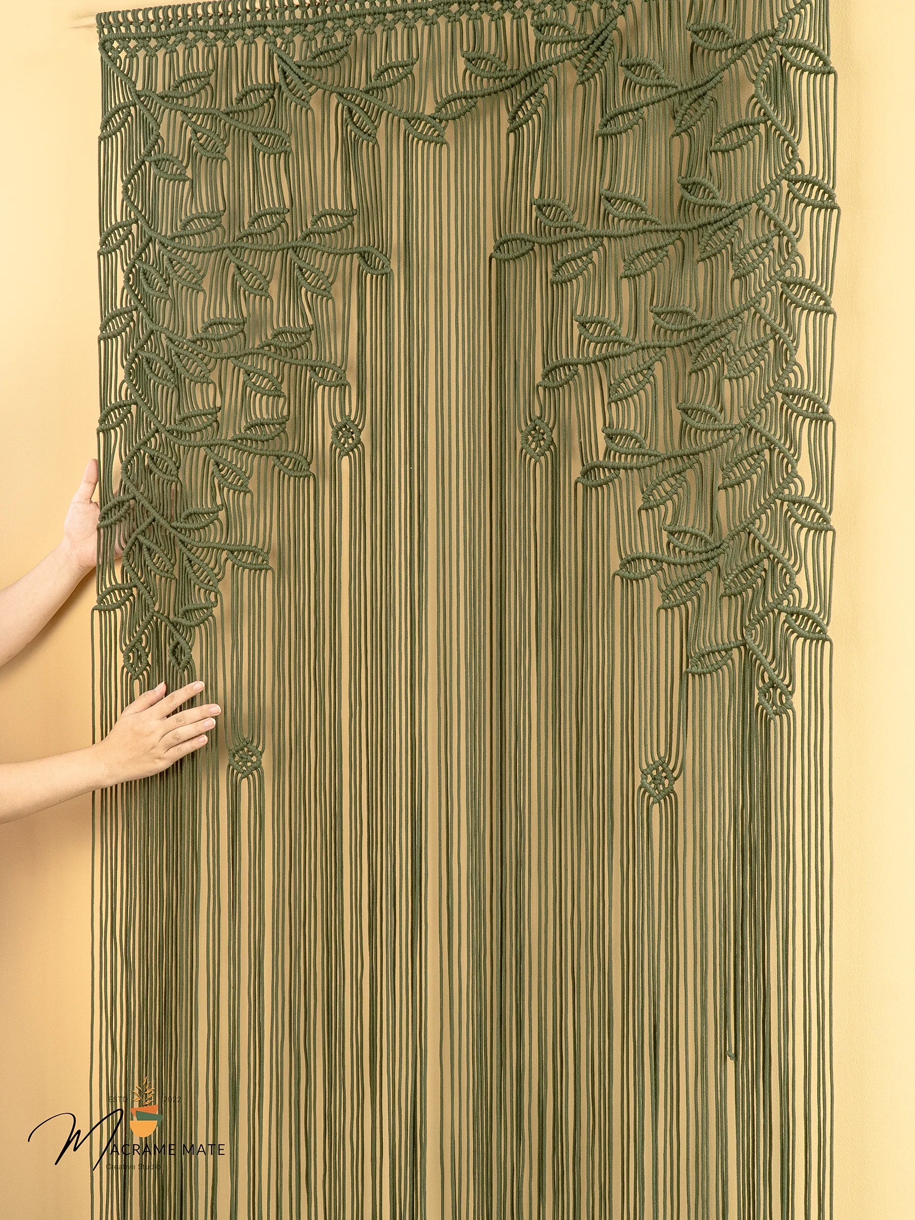 Decorative string curtain with leaf patterns held by a person against a beige background