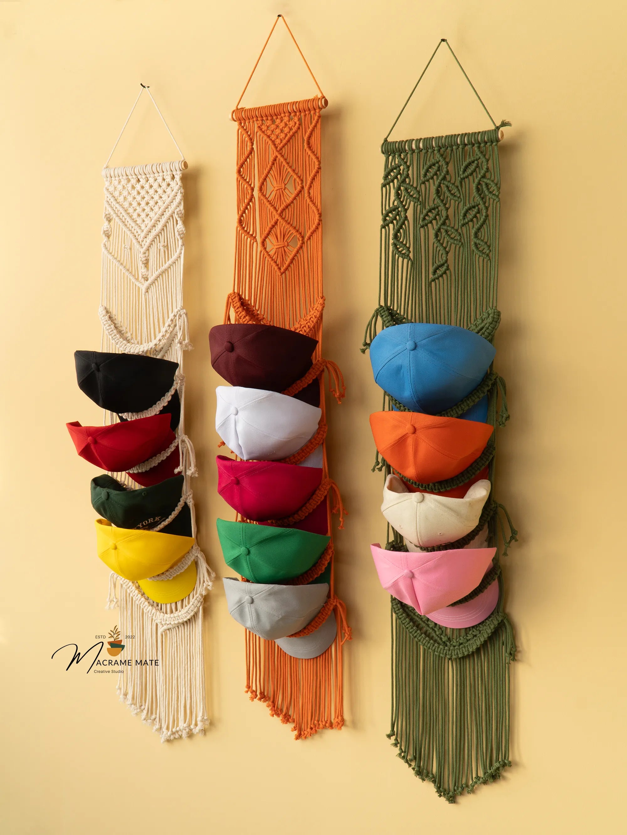 Three colorful macrame hat racks against a beige wall.