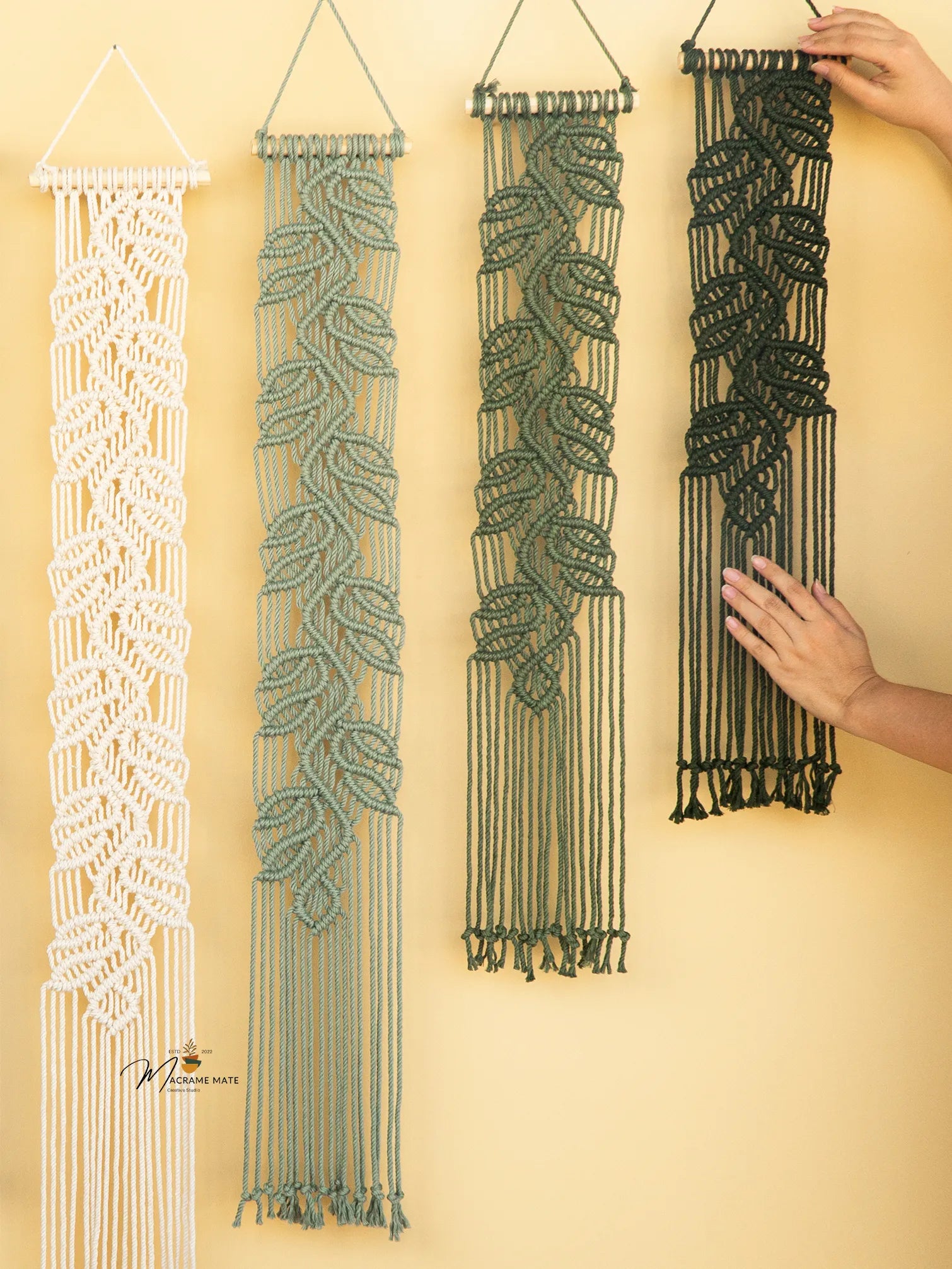 Four macrame wall hangings in different patterns on a yellow wall.