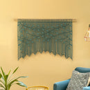 Decorative wall hanging with green leaves on a yellow wall, with a blue chair and plant in the foreground.
