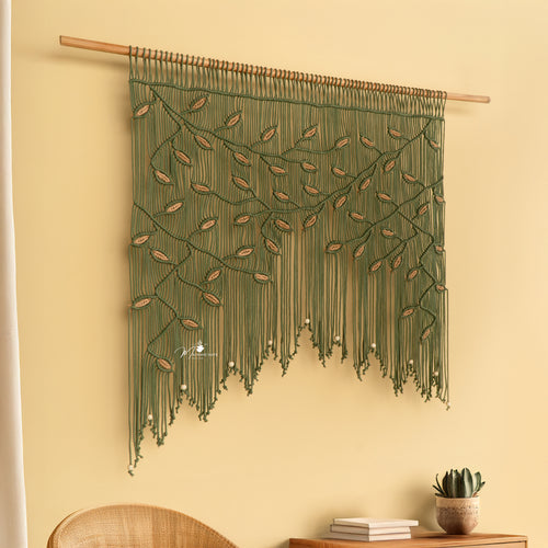 Decorative wall hanging with green strings and wooden rod on a beige wall.