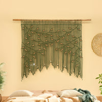 Decorative wall hanging with green and brown strings on a beige wall.