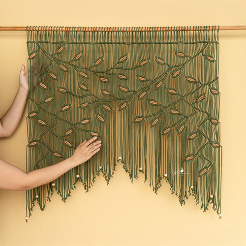 Handmade macrame wall hanging with green strings and wooden dowel on a beige background