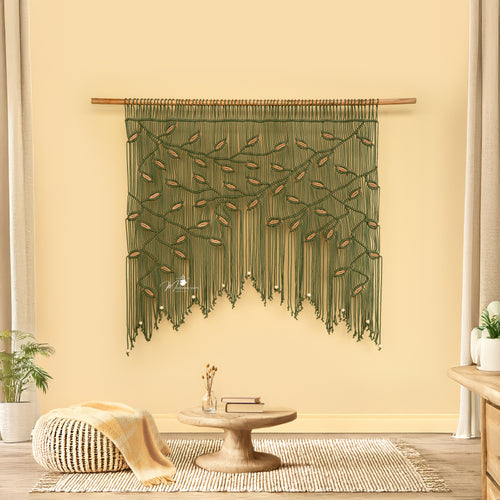 Decorative green wall hanging in a room with a table and plants.