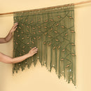 Handmade wall hanging with green yarn and wooden dowel on a beige background
