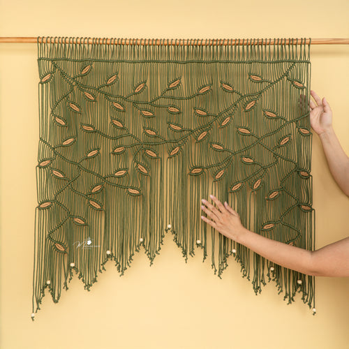 Handmade macrame wall hanging with green strings and wooden beads on a yellow background
