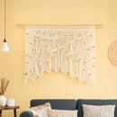 Macrame wall hanging on a yellow wall with a sofa and decorative items in the foreground