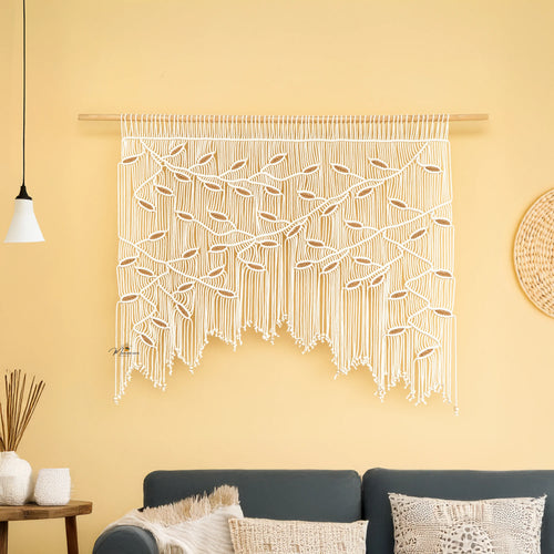 Macrame wall hanging on a yellow wall with a sofa and decorative items in the foreground