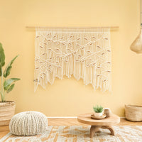 Macrame wall hanging on a yellow wall with a wooden coffee table and plants in a room.