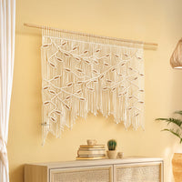 Macrame wall hanging with leaf pattern on a yellow wall above a cabinet.