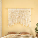 Macrame wall hanging with leaf pattern on a yellow wall above a bed.