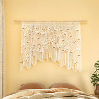Macrame wall hanging with leaf pattern on a yellow wall above a bed.
