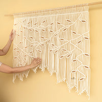 Macrame wall hanging with intricate patterns held by a person against a yellow background