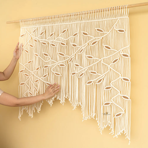 Macrame wall hanging with intricate patterns held by a person against a yellow background