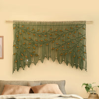Decorative wall hanging with green leaves on a beige wall above a sofa.