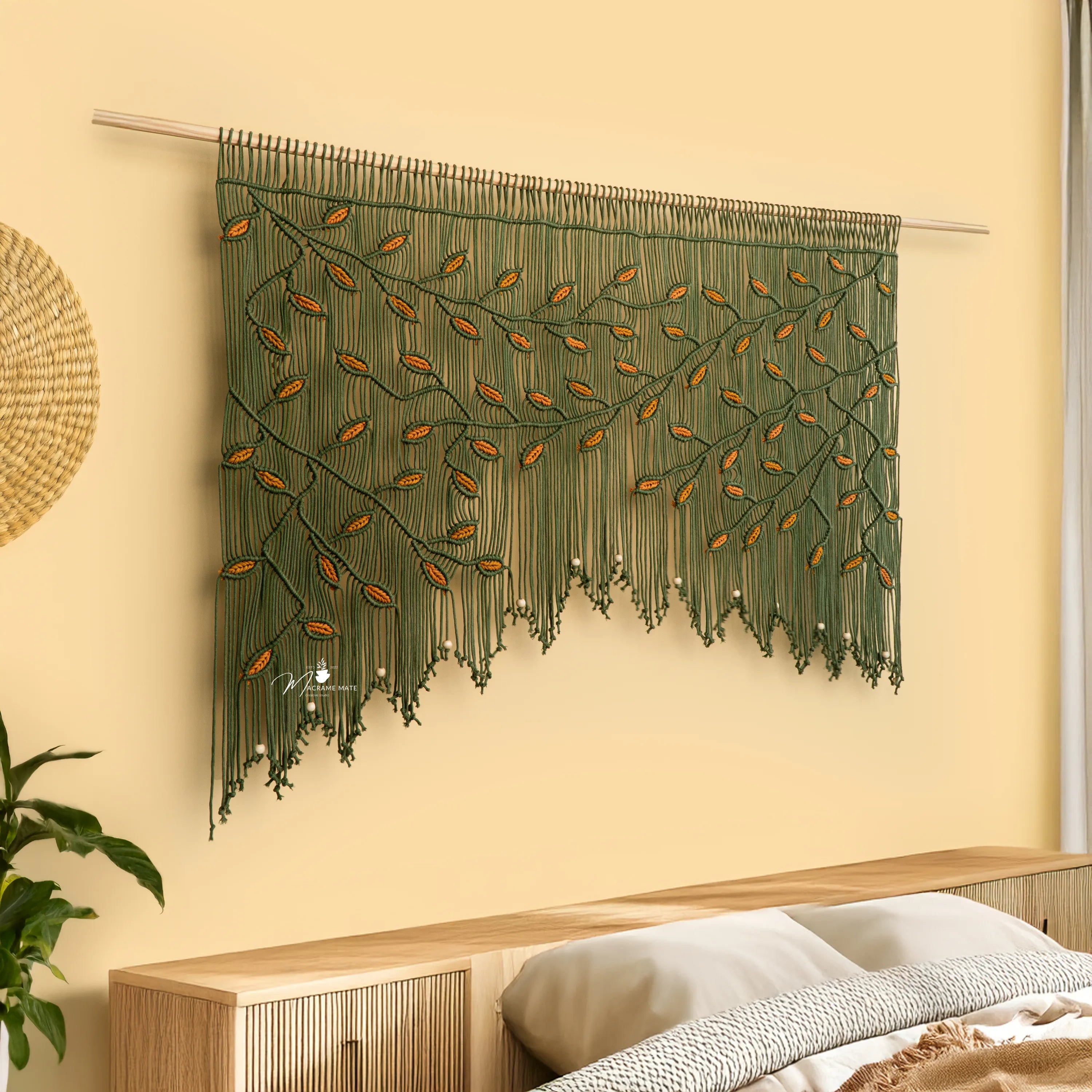 Decorative wall hanging with leaf pattern on a light yellow wall above a wooden shelf.