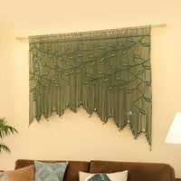 Decorative green wall hanging with leaf pattern on a beige wall above a brown sofa.