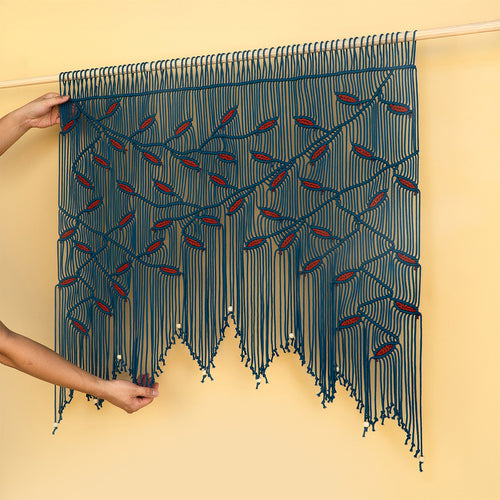 Handmade woven textile with red accents held by a person against a beige background