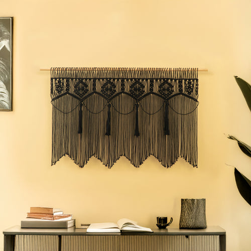 Decorative black lace curtain hanging on a yellow wall with a shelf below.