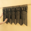 Black macrame wall hanging with tassels on a yellow background