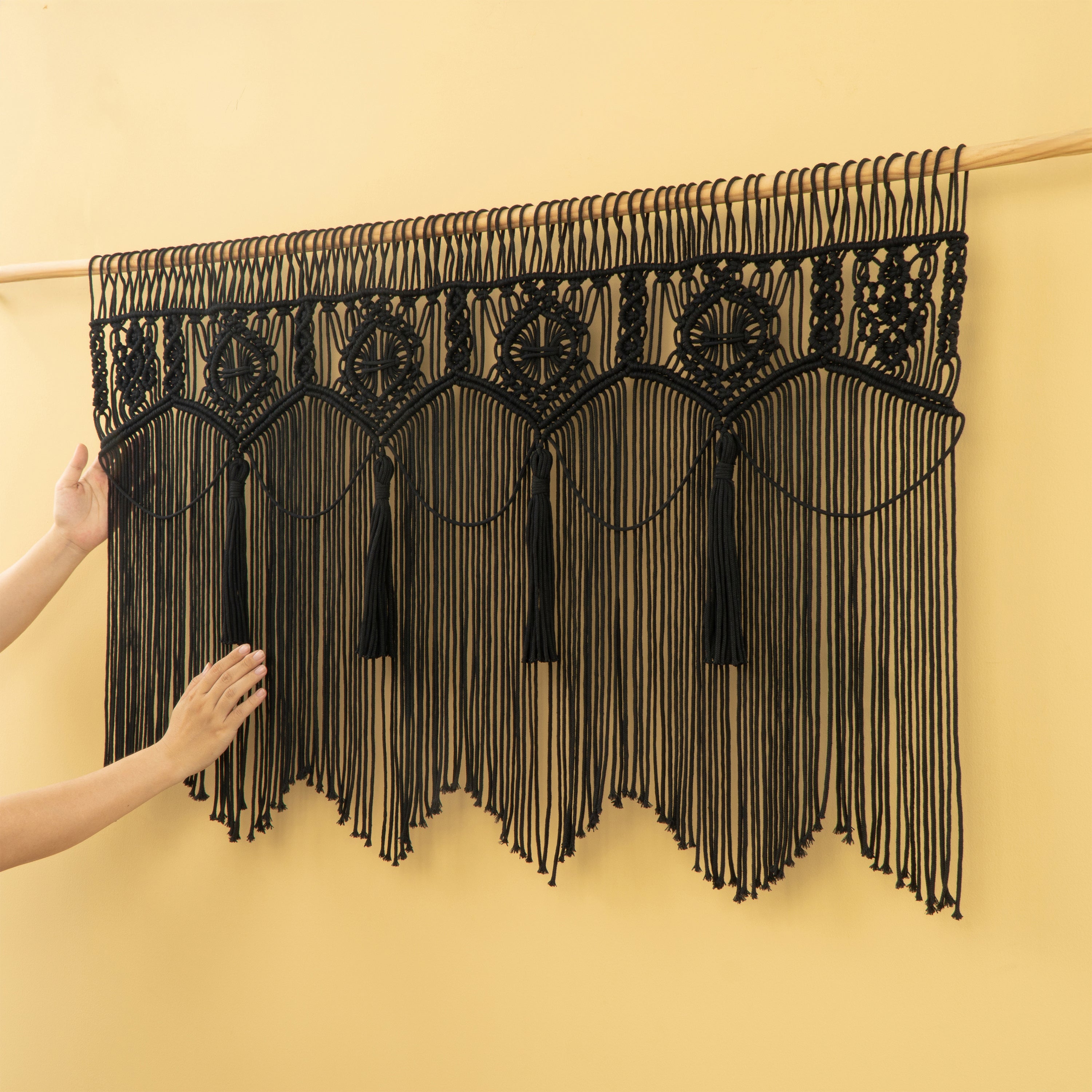 Black macrame wall hanging with tassels on a yellow background