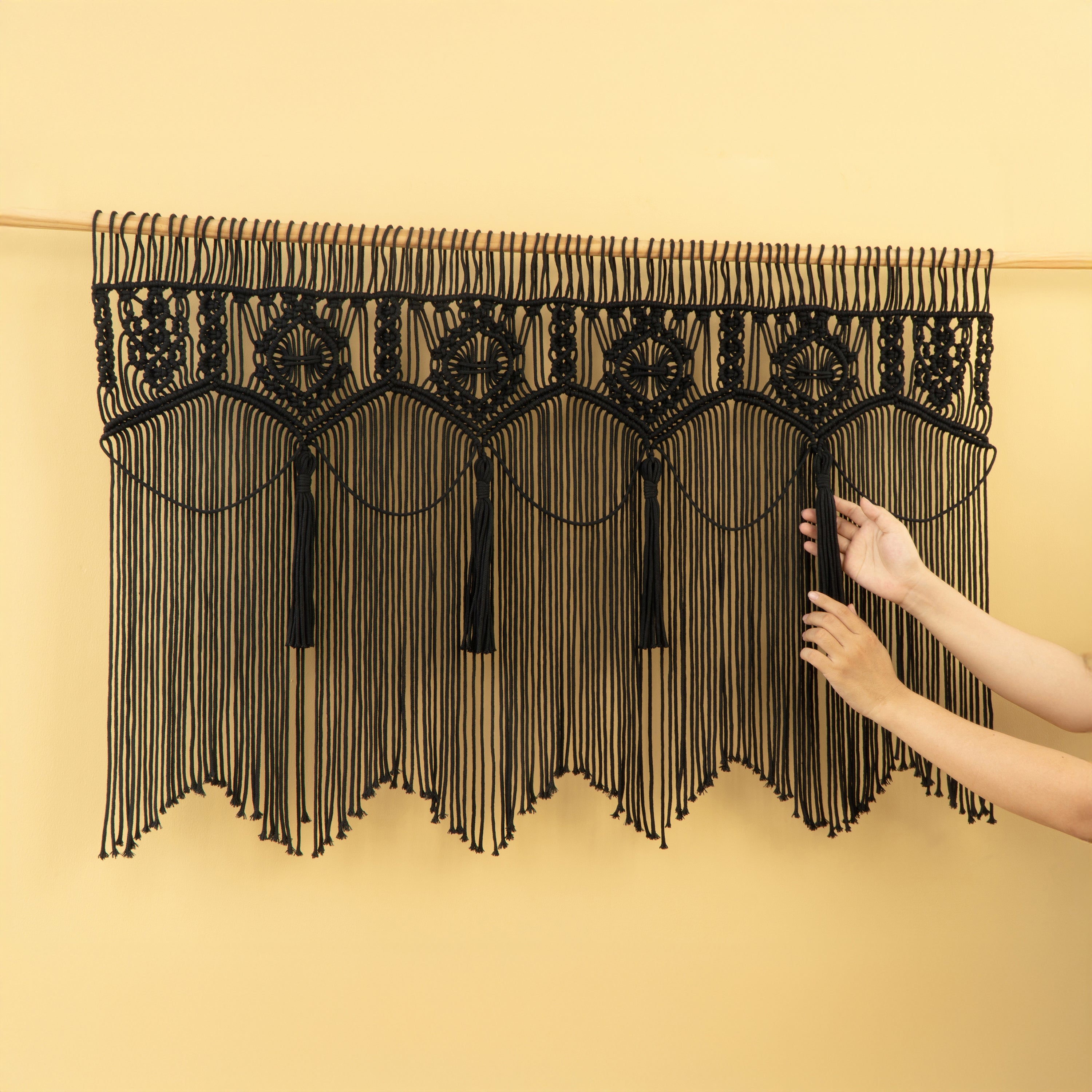 Black macrame curtain with geometric patterns on a beige background
