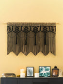 Decorative black lace valance hanging on a yellow wall above a dark cabinet with candles and framed pictures.