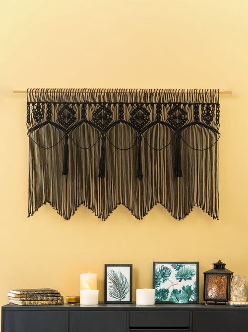 Decorative black lace valance hanging on a yellow wall above a dark cabinet with candles and framed pictures.
