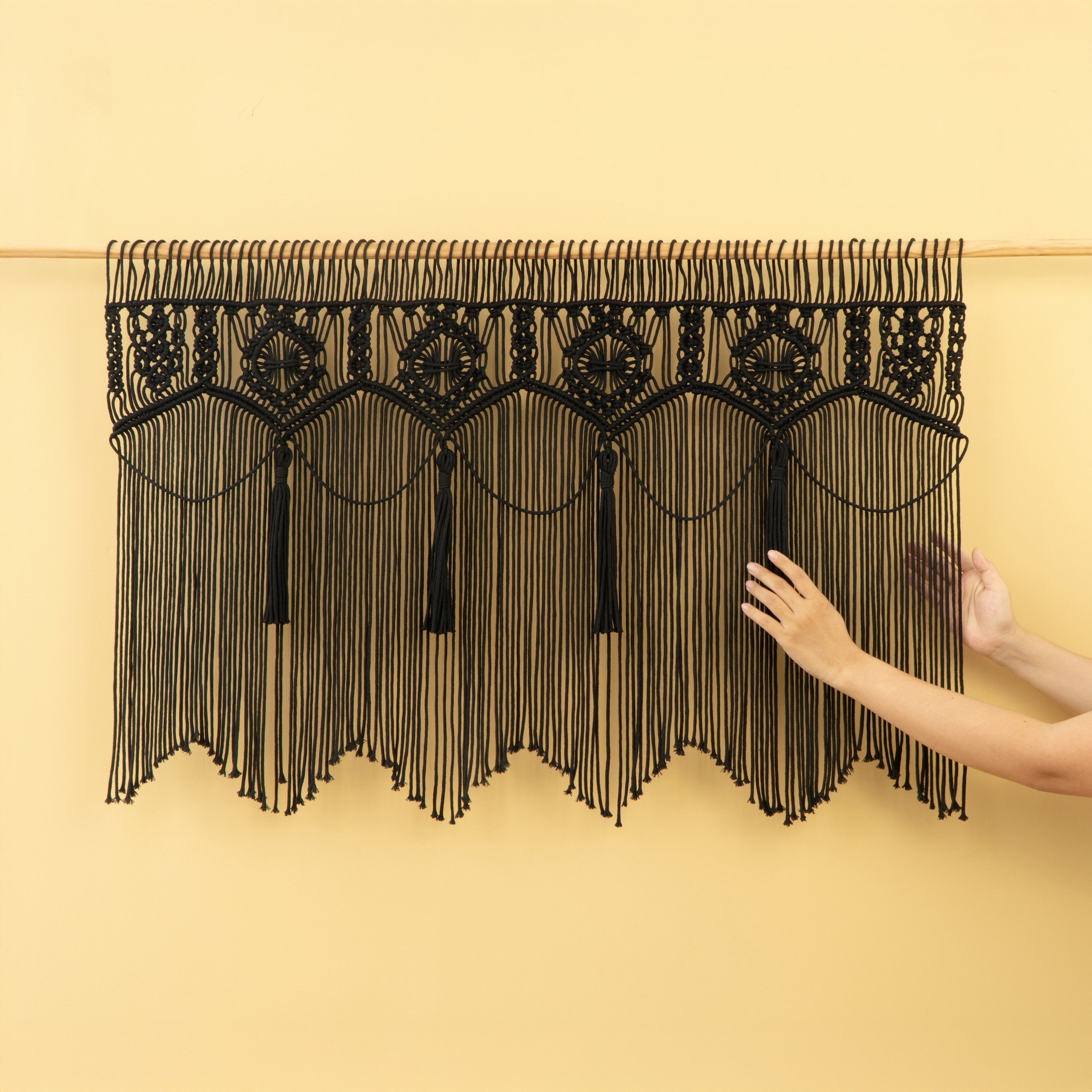 Black macrame wall hanging with tassels on a beige background