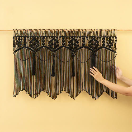 Black macrame wall hanging with tassels on a beige background
