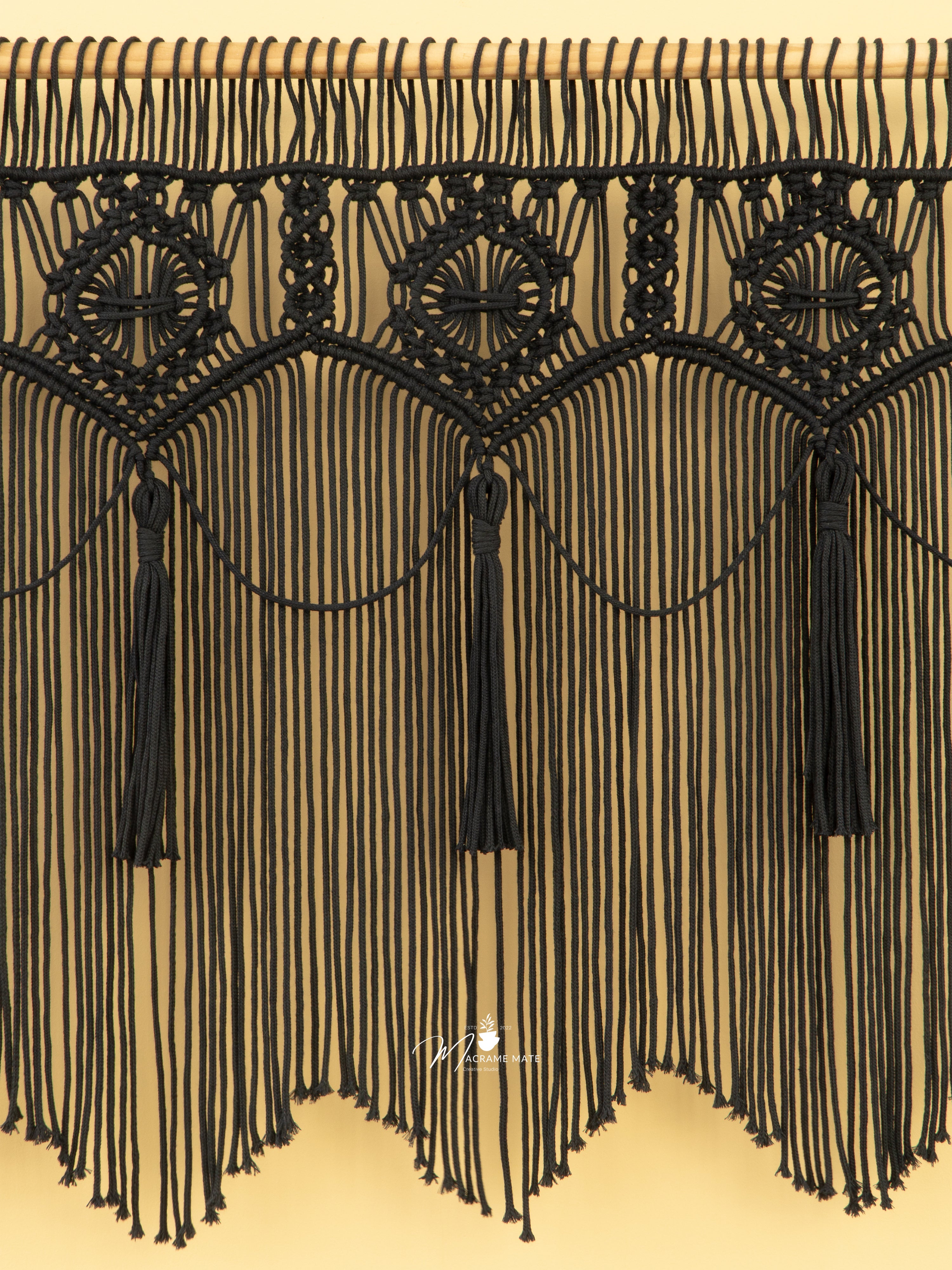 Black macrame wall hanging with tassels on a beige background