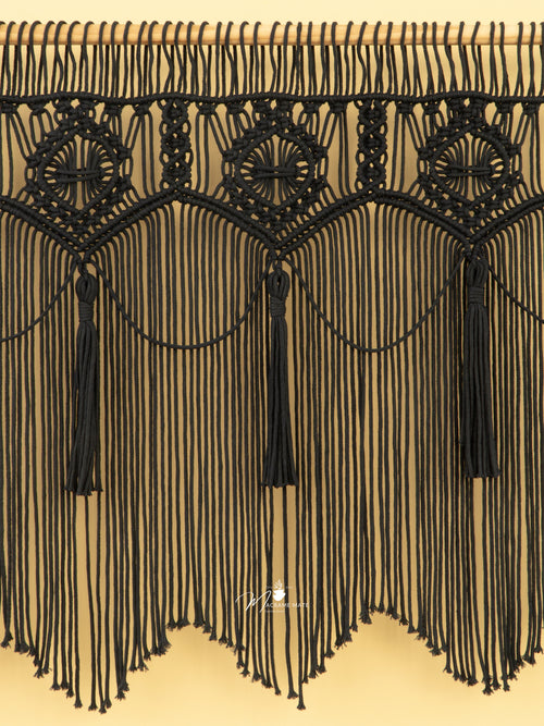 Black macrame wall hanging with tassels on a beige background