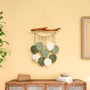 Decorative wall hanging with leaves on a yellow wall above a wooden cabinet.