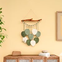 Decorative wall hanging with leaves on a yellow wall above a wooden cabinet.