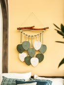Decorative wall hanging with leaf-shaped beads on a yellow wall.