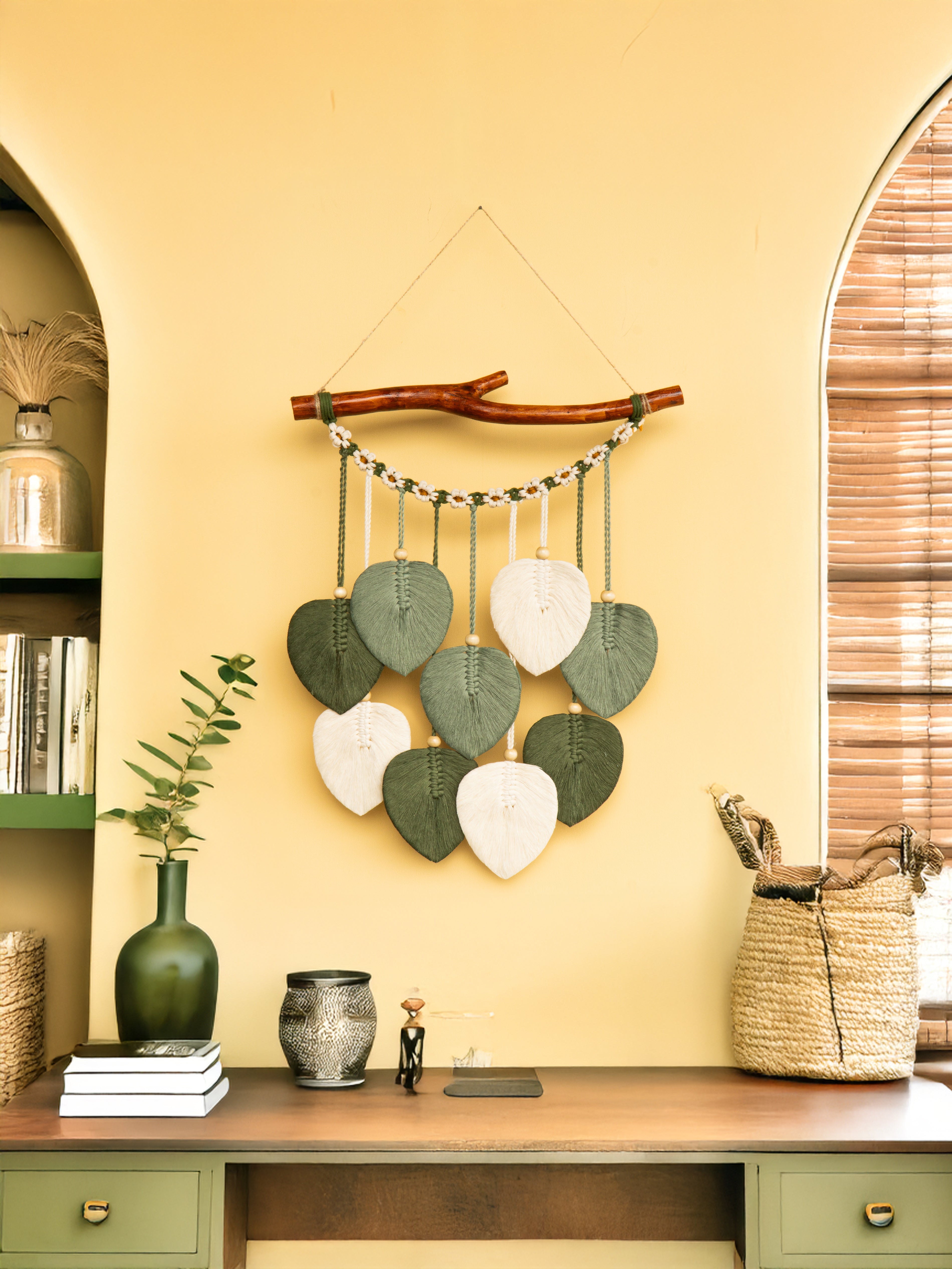 Decorative wall hanging with green and white leaves on a yellow wall.