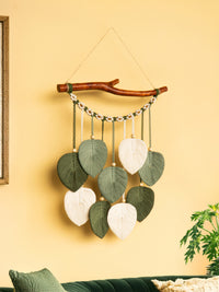 Decorative wall hanging with leaves and a branch on a yellow wall.