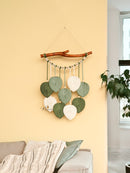 Decorative wall hanging with leaf-shaped stones and a branch on a yellow wall.