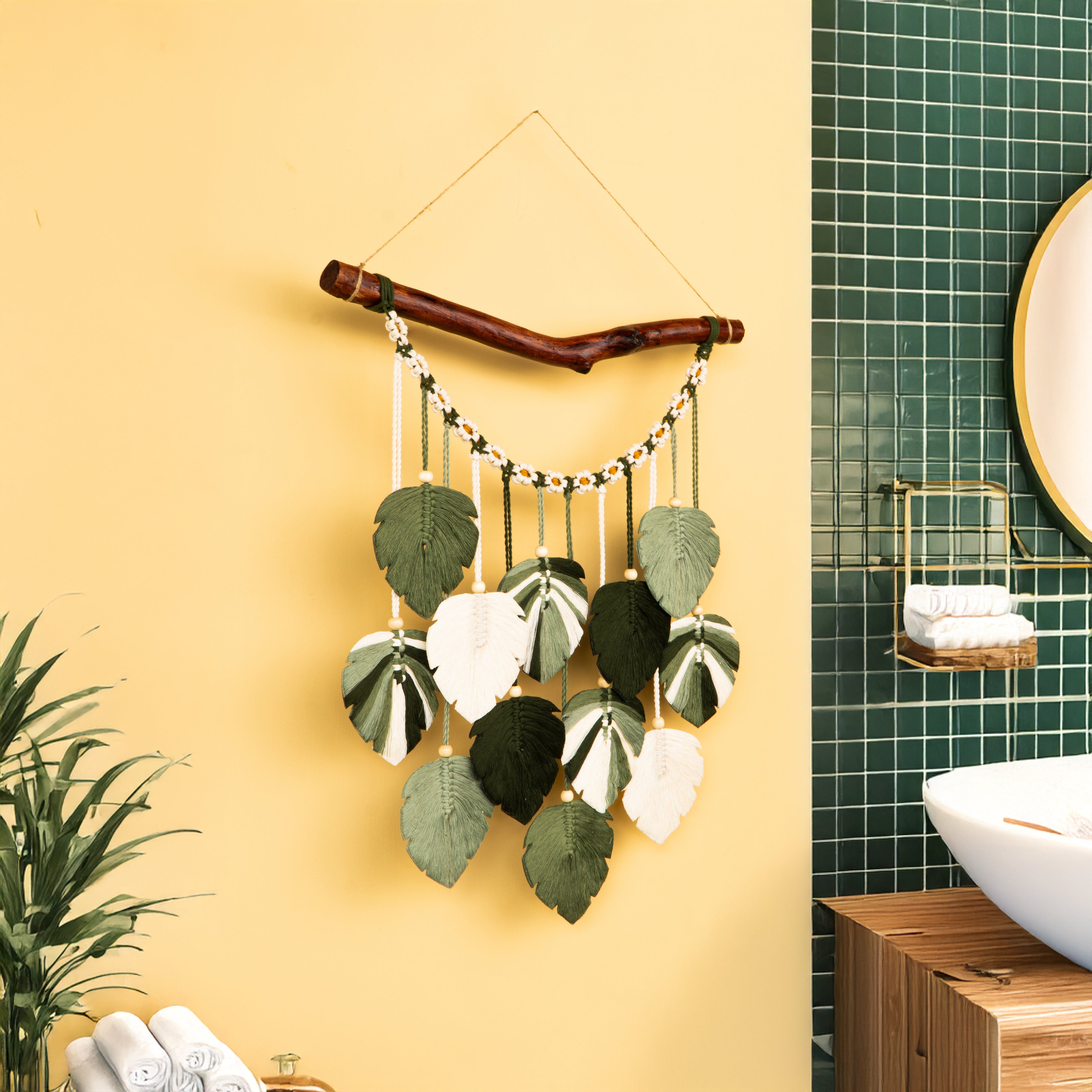 Decorative wall hanging with leaves on a yellow wall next to a bathroom with green tiles.