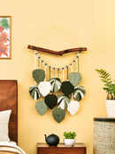 Decorative wall hanging with leaf patterns on a yellow wall above a wooden dresser.