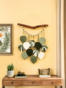 Decorative wall hanging with leaf patterns on a yellow wall above a wooden desk.