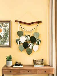 Decorative wall hanging with leaf patterns on a yellow wall above a wooden desk.