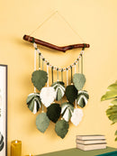 Decorative wall hanging with leaves and a branch against a yellow wall.