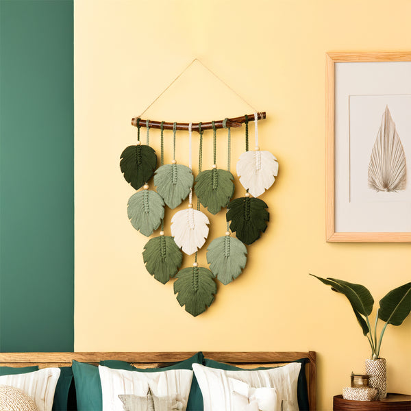 Decorative wall hanging with leaf-shaped objects on a yellow wall with a framed picture.