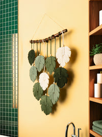 Decorative wall hanging with green and white leaves on a yellow wall.
