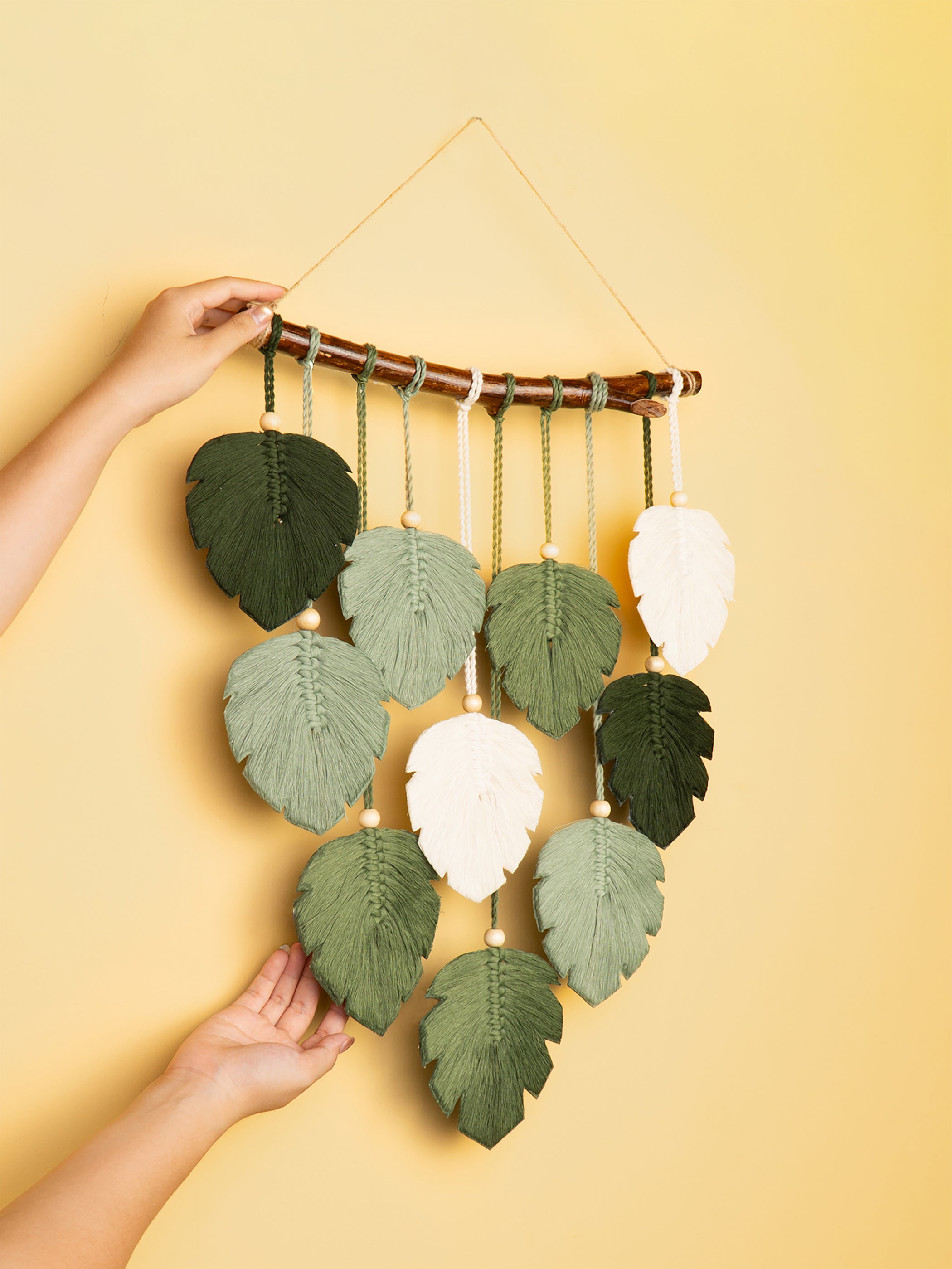 Handmade leaf-shaped wall hanging with green and white leaves on a yellow background