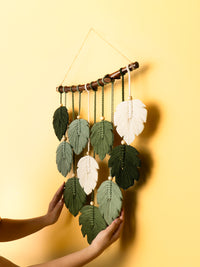Handmade leaf-shaped wall hanging with green and white leaves on a yellow background
